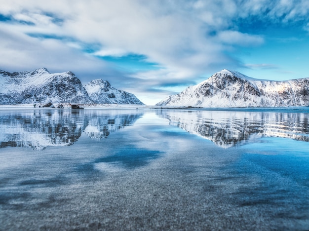 Landscape with snowy mountains, sea, blue sky with clouds reflected in water in winter