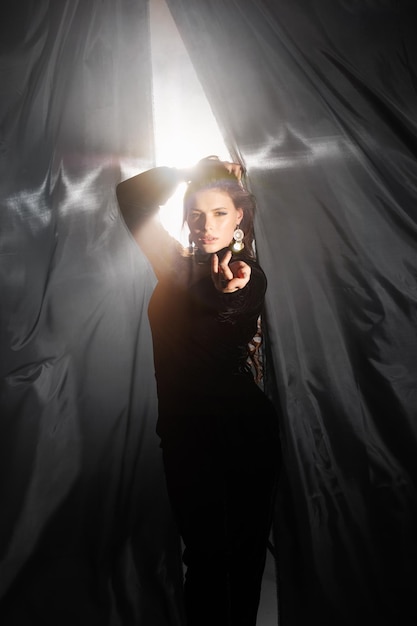 Languid young woman in elegant long dress leans against black curtain in studio