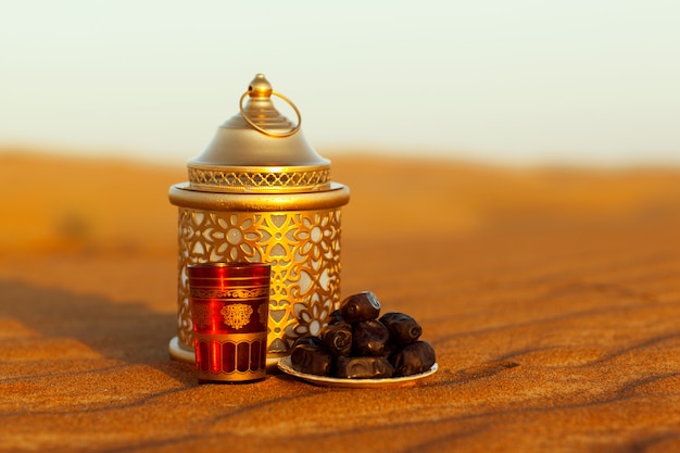 Lantern, cup and dates are on the sand in the desert 