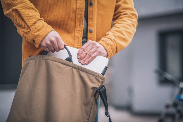 Laptop in bag. Close up of mans hand putting laptop into a bag