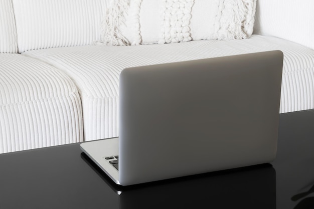 Laptop on a black glass table against a white sofa Back view The screen is not visible