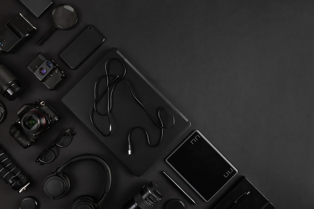 Laptop and camera equipment arranged on black abstract desk background with empty space. Photographer workplace concept.