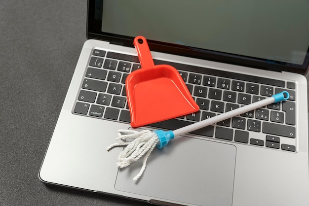 Laptop cleaning concept Small toy shovel and mop on laptop keyboard Online cleaning service