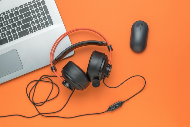 Laptop computer mouse and black and orange headphones on an orange background Creative workplace