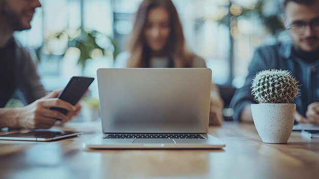 A laptop computer on a table with blurred people in the background and a cactus in the foreground