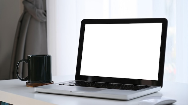 Laptop computer with blank white screen and coffee cup on white table