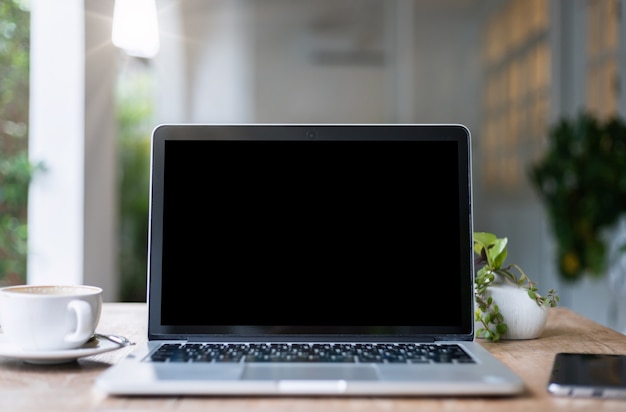 laptop computer with empty screen with coffee cup and smartphone on table of the coffee