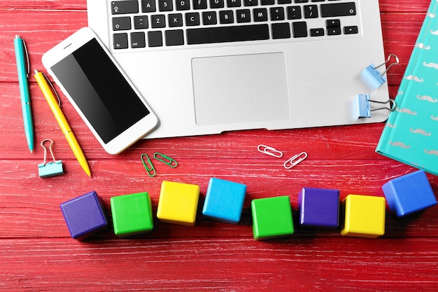 Laptop copybook and wooden cubes on color background