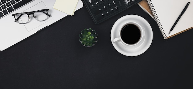 Laptop glasses coffee cup and calculator on a black background top view