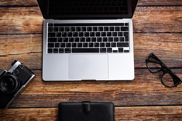 Laptop, glasses, notepad and a cup of coffee on a wooden table top view