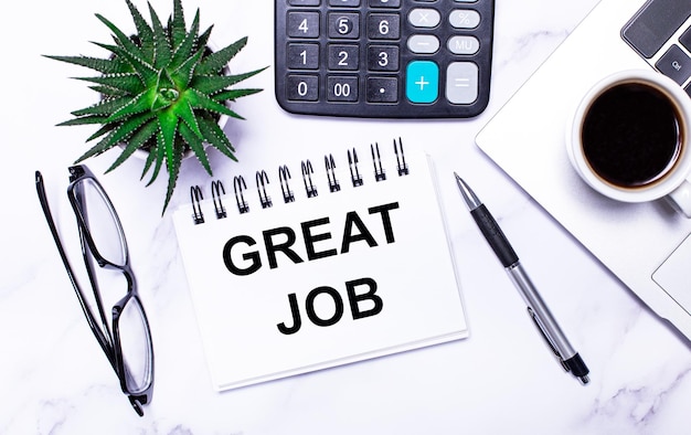 A laptop glasses a pen a calculator a cup of coffee a green plant and a white notepad with the text GREAT JOB lie on a table with task lighting View from above Business concept