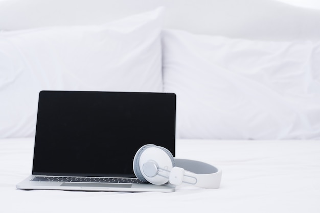 Laptop and headphone on the white bed.