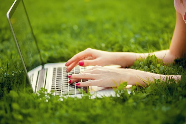 The laptop is on the grass and female hand close-up