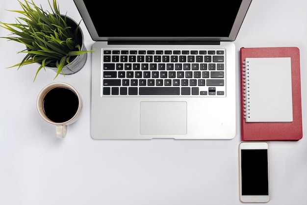 Laptop and note book with a mobile phone on white desk