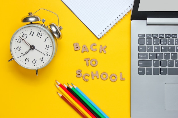 Laptop and notebook with colored pencils near a clock