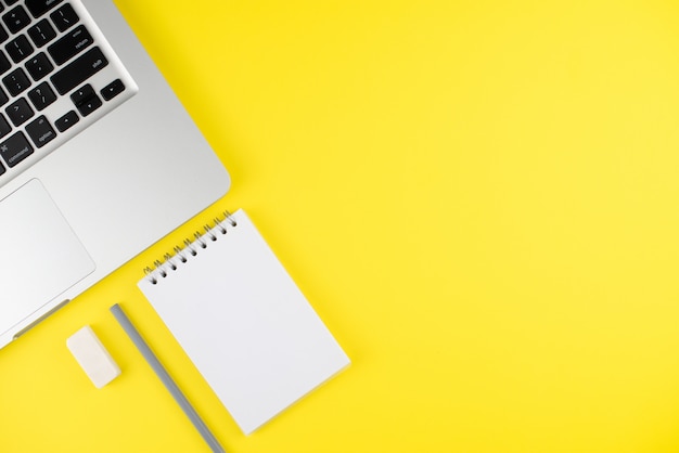 Laptop, notepad planner with gray pencil and erase rubber on yellow background. Flat lay. Copy space. 