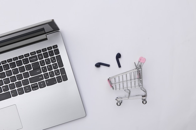 Laptop and shopping trolley with wireless headphones on white background. Top view