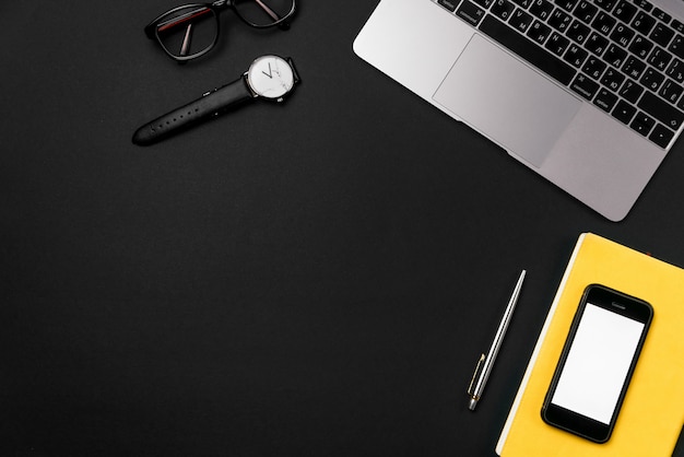 Laptop, smart phone, glasses and watch on black office desk.