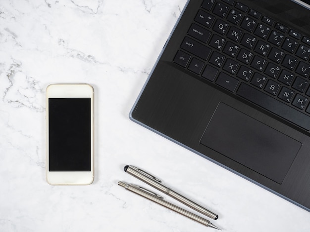 Laptop smartphone and silver pen on the marble table top view copy space