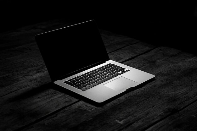 Photo a laptop on a table in a dark room with a lamp hanging on the wall