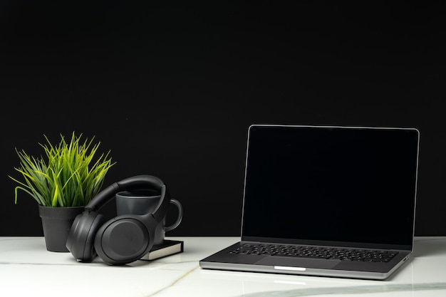 Laptop with black screen on working desk with cup and earphones on black background