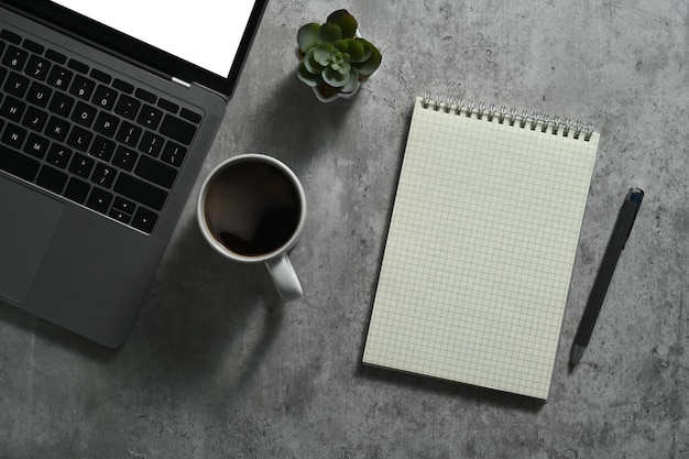 Laptop with blank screen cup of coffee and notebook on concrete stone office desk Top view with copy space