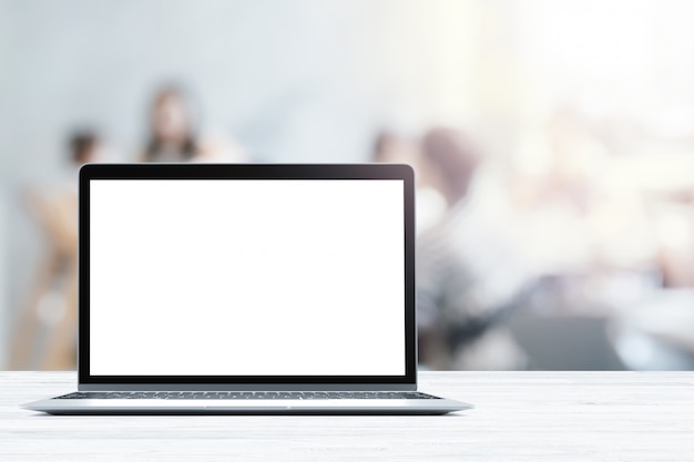 Laptop with blank screen placed on white wooden table in blurred people in coffee shop or restaurant