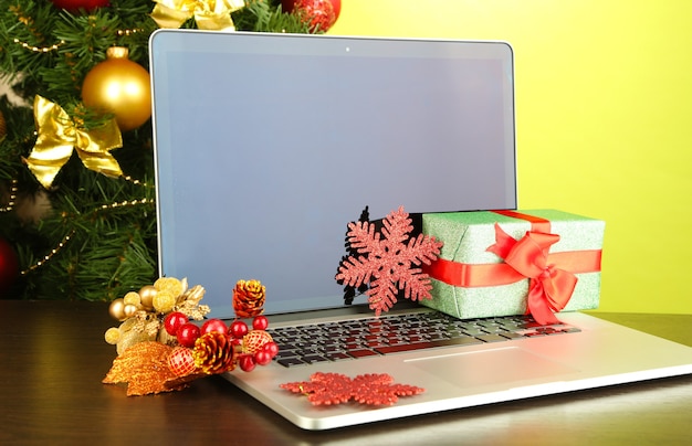 Laptop with gifts on table on green background