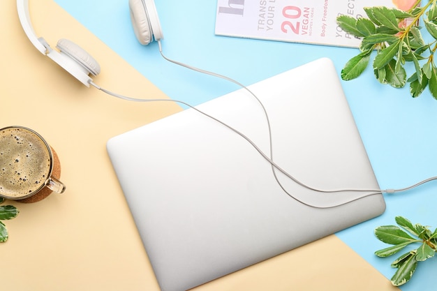 Laptop with headphones and cup of coffee on blue and orange, top view