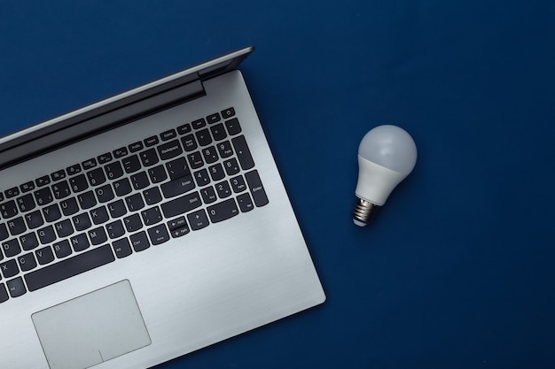 Laptop with LED light bulb on classic blue background. Color 2020. Top view