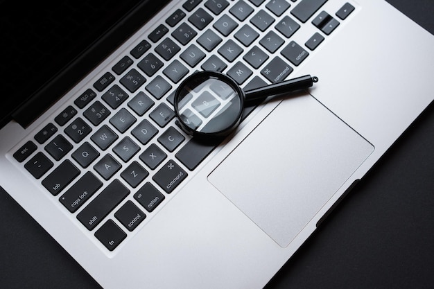 Laptop with magnifying glass on dark office table, concept of search