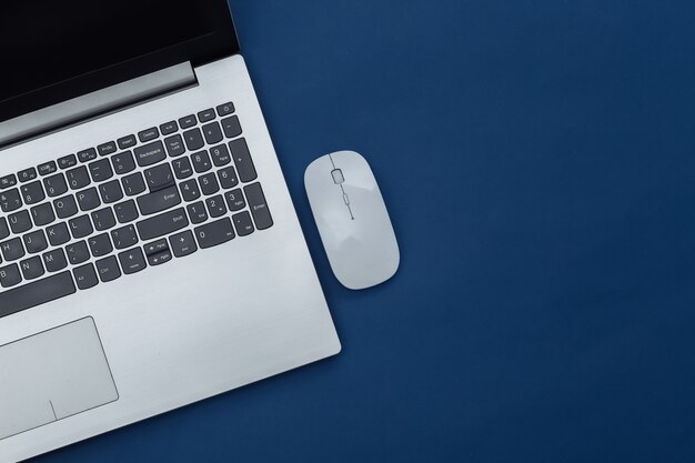 Laptop with pc mouse on classic blue background. Online workspace. Remote work. Studio shot. Color 2020. Top view. Flat lay