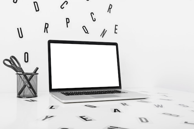 Laptop with pencil holder and many alphabets on white backdrop