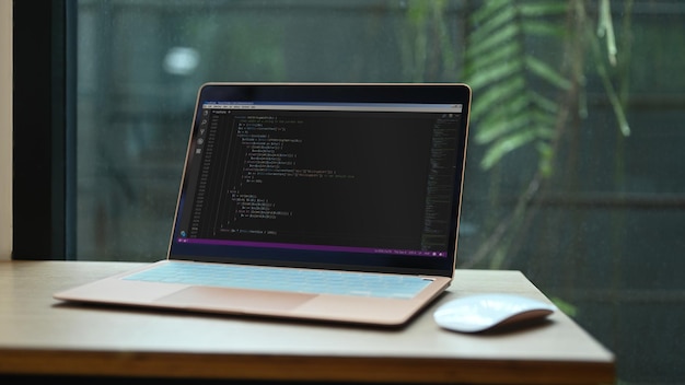 Laptop with programming code on screens and wireless mouse wooden office desk at software development company