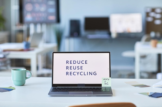 Laptop with slogan of sustainable life on blank screen standing on workplace of manager in office of