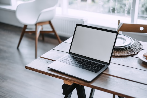 Laptop with a white screen on the rustic wooden table in the kitchen room.