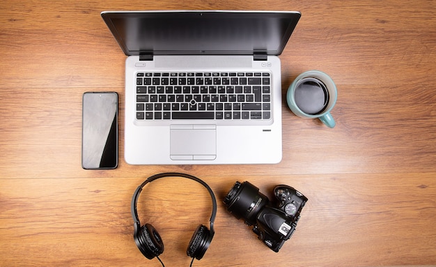 laptop on wooden desk with a cup of coffee headphones a dslr camera and a celular phone smartphone