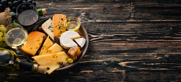 A large assortment of cheeses brie cheese gorgonzola blue cheese grapes honey nuts red and white wine on a wooden table Top view Free space for text