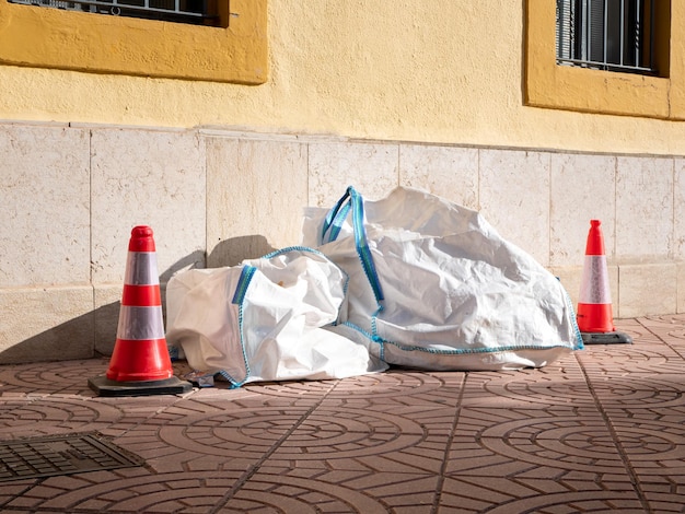 Large bags of construction debris lie next to the wall of the building and are fenced with restrictive cones