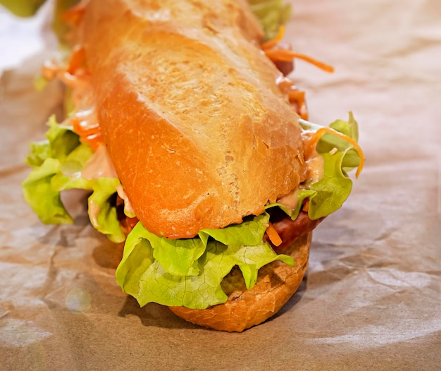 Large baguette sandwich with salami lettuce cheese and sauce Close up Selective focus