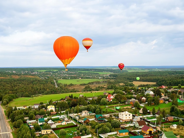 Large beautiful hot balloons fly high in sky over scenery green field and forest