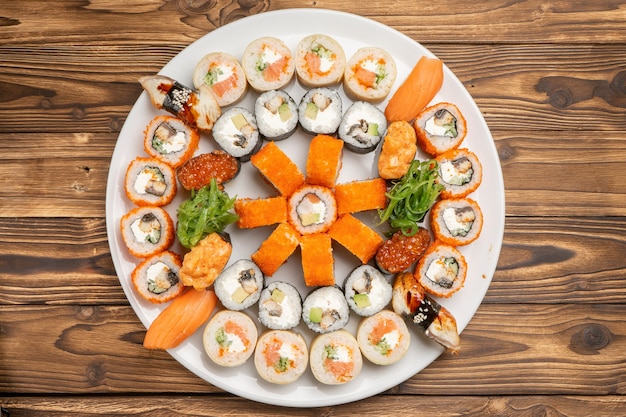 A large beautiful sushi set with maki rolls, nigiri and gunkans on a white round ceramic plate