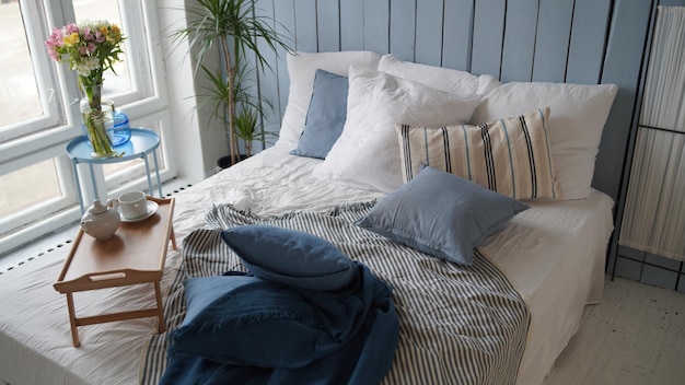 Large bed with pillows and blankets Wooden stand for breakfast on crumpled bed in studio Closeup of interior design room