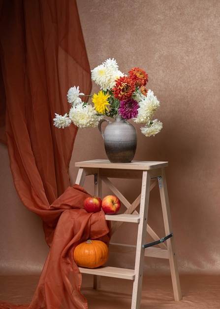 A large bouquet of Asters flowers in a vase on a wooden staircase two red apples a small pumpkin