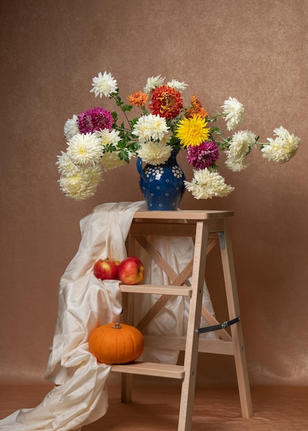 A large bouquet of dahlias on a wooden staircase Below are two red apples and a pumpkin White scarf 