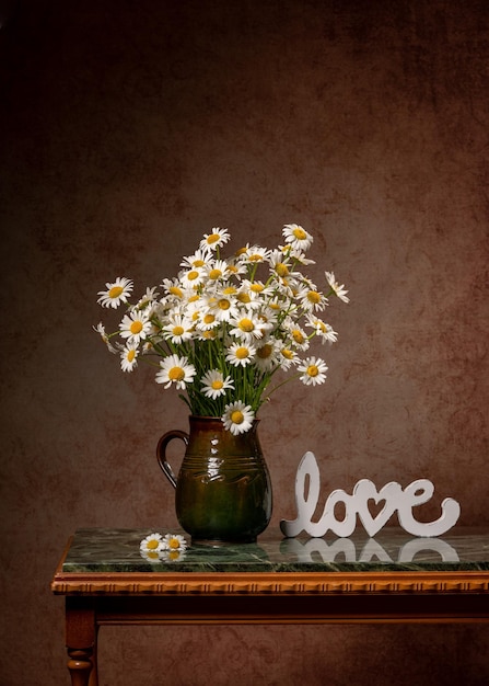 A large bouquet of white daisies in a brown clay jug on a marble green table White inscription love