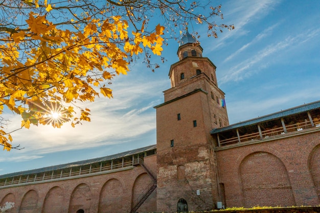 A large brick building with a tower and a tree with yellow leaves in front of it