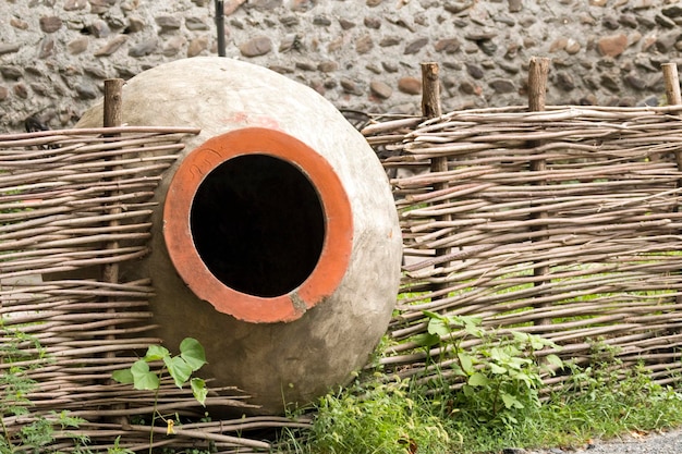 Large ceramic vessel for wine and wicker fence on a background of a stone wall