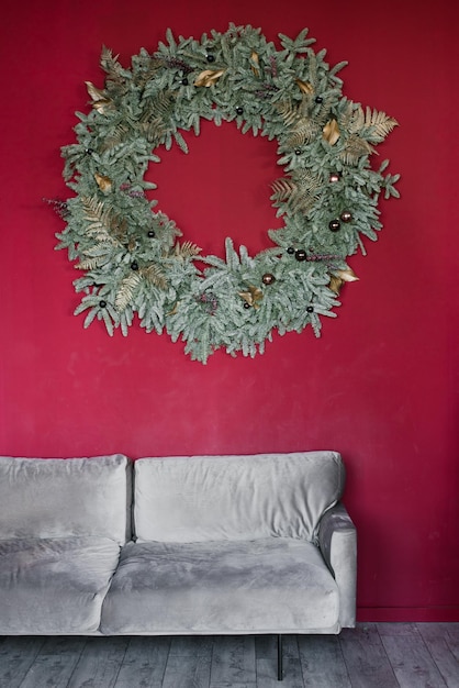 Large christmas wreath hanging on burgundy wall above gray sofa in living room