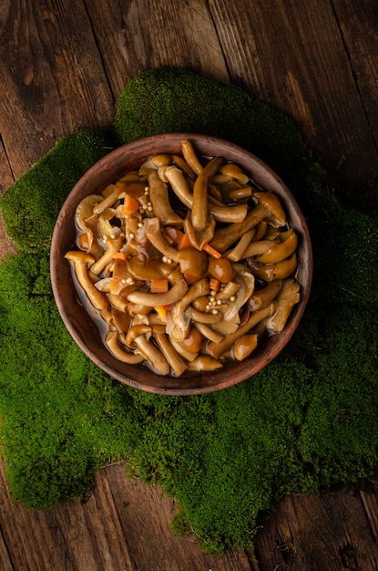 Photo a large clay bowl with wild mushrooms (honey mushrooms), stands on an old wooden table with green moss. eco products, natural gathering